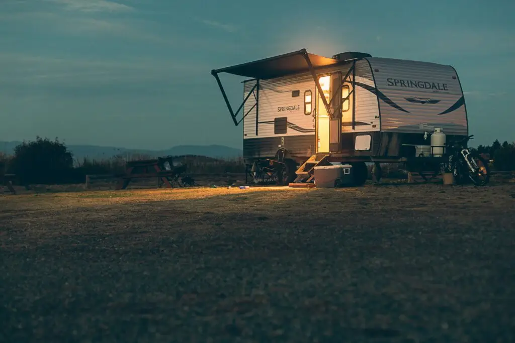 A caravana and camping setup at dusk with lights on inside.